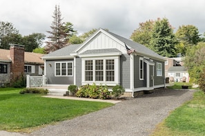 Une maison de plain-pied à l’extérieur gris et aux ornements blancs, dotée d’un porche à l’avant et d’un petit jardin.