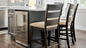 Una cocina con armarios blancos, un refrigerador de acero inoxidable, una isla de madera con sillas y una lámpara colgante.