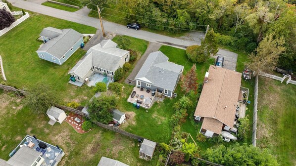 A residential area with three houses, each with a distinct roof style and surrounded by lawns and trees.