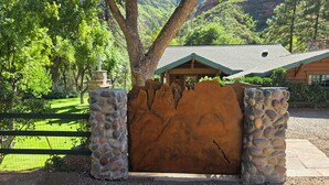 Entrada rústica a una cabaña con una puerta de piedra, rodeada de un paisaje verde exuberante y montañas al fondo.