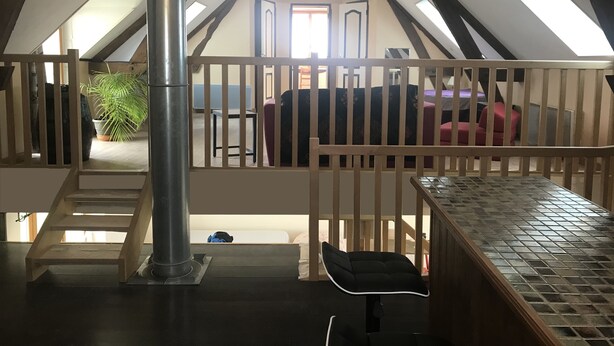 Ein Schlafzimmer im Dachgeschoss mit schrägen Wänden, einer Holztreppe, einem Metallheizkörper und Blick auf den Wohnbereich darunter.
