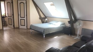 Ein Schlafzimmer mit Schlafgalerie, einem Bett mit kariertem Überwurf, einem Standventilator und einem Ledersofa.
