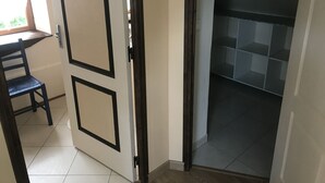 Ein Zimmer mit geschlossener Tür, einem Fenster, einem Sessel und einem Fliesenboden.