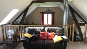 Ein Loft-Zimmer mit schwarzem Leder-Sofa, Holzboden, einem Esstisch mit Stühlen, einem Ventilator und einem Kamin.