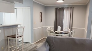 Ein Wohnzimmer mit grauem Sofa, einem Esstisch mit Stühlen und einer Küchenzeile.