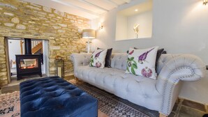Una sala de estar con pared de piedra, un sofá con cojines decorativos, un otoman azul, una lámpara de pie y una chimenea.