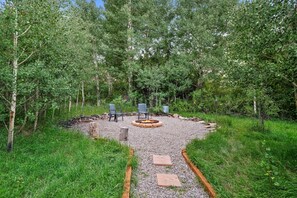 Sit by the fire pit in a serene wooded setting, surrounded by a gravel path and comfortable seating for two.