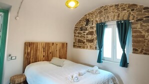 A bedroom with a wooden headboard, a stone arch wall, a window with curtains, a patterned floor, and a hanging light fixture. - Two Bedroom Apartment (Bordighera)