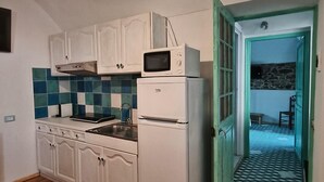 A compact kitchen with white cabinets, a microwave, and a refrigerator. There's a wooden floor and a tiled backsplash. - Two Bedroom Apartment (Bordighera)