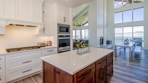 Une cuisine spacieuse avec des meubles blancs, un grand îlot central et une vue sur l’extérieur.