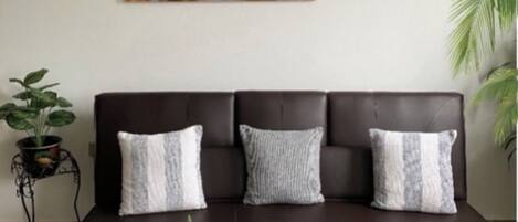 A dark brown sofa with three white cushions, a Buddha painting above it, and a potted plant to the left.