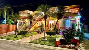 A two-story house with a well-lit entrance, a staircase, and a small garden area with palm trees.