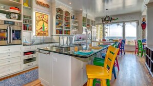 A spacious kitchen with white cabinetry, a central island, and colorful chairs. - Casa Banana Oceanfront on Ocean Blvd, 6 BD, sleeps 20, pool,hot tub, elevator (Isle Of Palms)