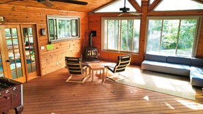 Cozy cabin-style room with a high ceiling, large window, and wood stove.