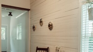 Una zona de menjador amb taula i cadires de fusta, parets amb panells blancs i un llum penjant.