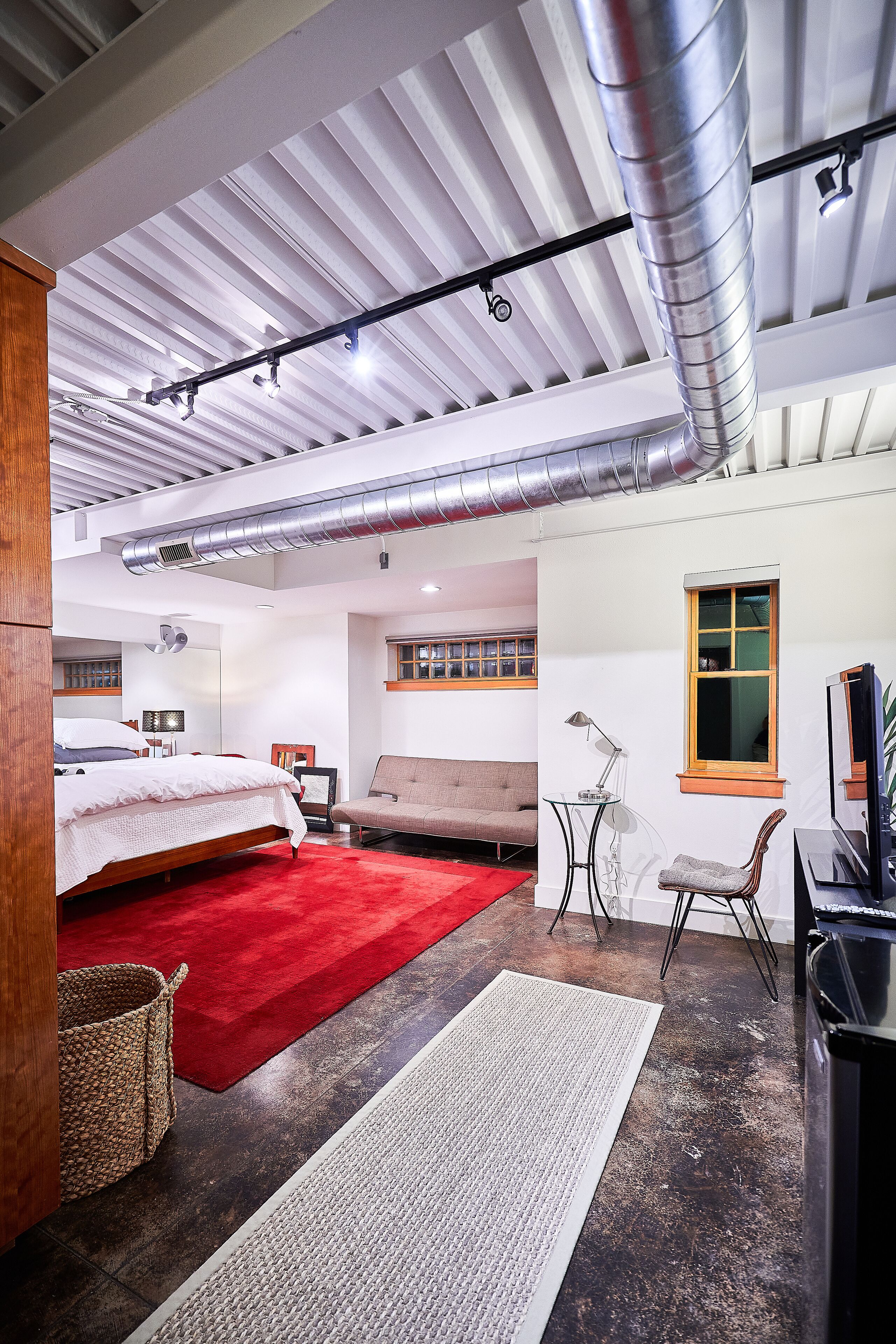 Un dormitorio moderno con una cama grande, una alfombra roja, un escritorio con lámpara y un televisor.