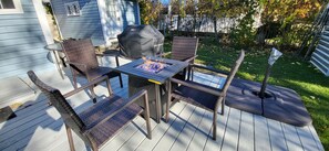 A deck with a table and four wicker chairs, a barbecue grill, and a small fire pit.