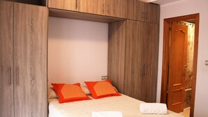 A bedroom with a bed, two orange pillows, a white towel, and wooden wardrobe cabinets. - APARTMENT 2 MINUTES AWAY FROM PUERTA DEL MAR BEACH  (Almuñécar)