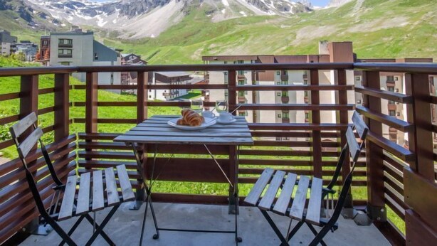 A balcony with a table and chairs, overlooking a mountainous landscape with buildings in the background. - Le Curling B (Val Claret) by Interhome (Tignes)