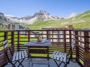 A balcony with a table and chairs, overlooking a mountainous landscape with buildings in the background. - Le Curling B (Val Claret) by Interhome (Tignes)