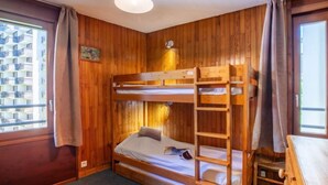 A bunk bed room with wooden walls, a ceiling light, and a window with curtains. - Le Curling B (Val Claret) by Interhome (Tignes)