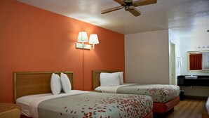 A hotel room with two beds, a ceiling fan, a bathroom with a sink and mirror, and a red wall.
