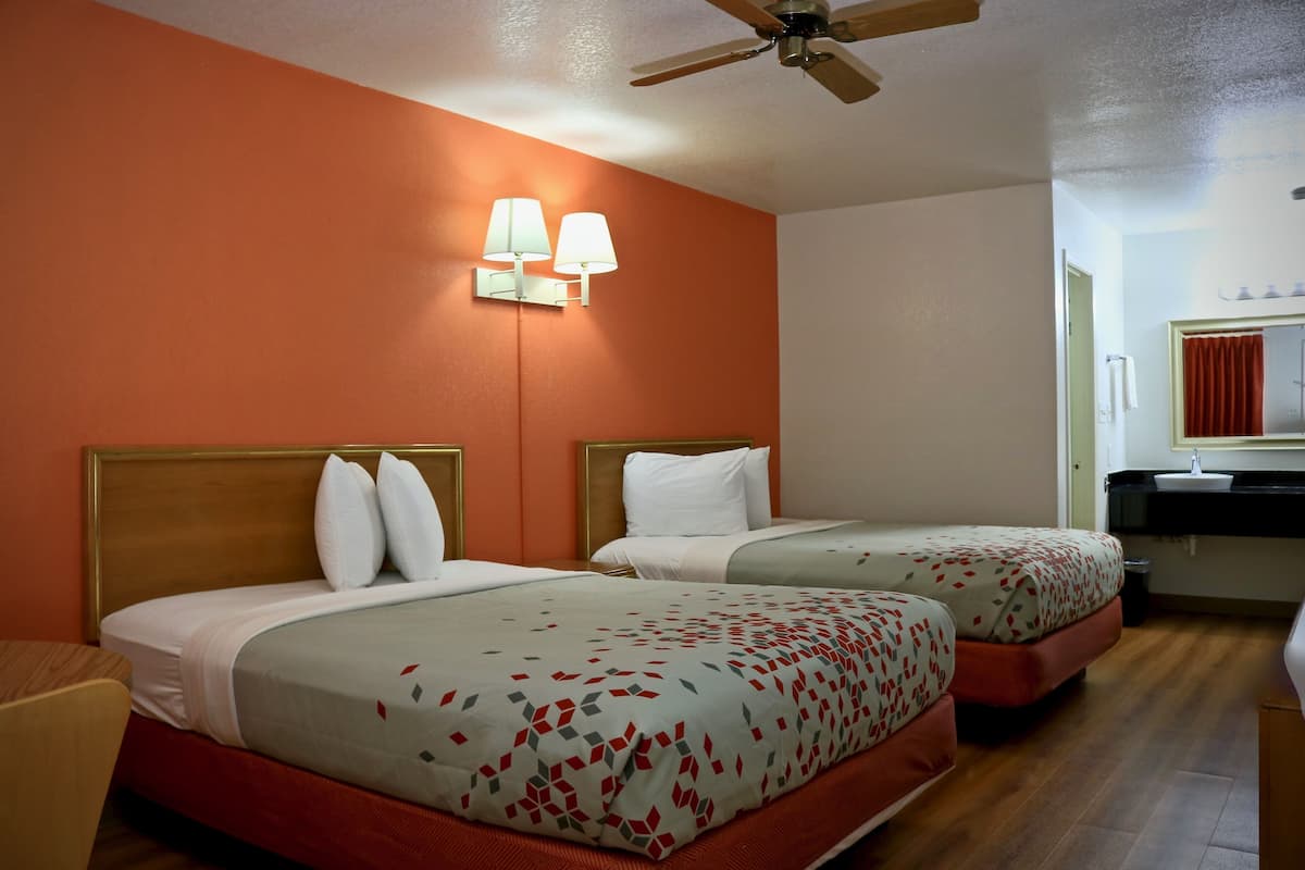 Ein Hotelzimmer mit zwei Betten, einem Deckenventilator, einem Badezimmer mit Waschbecken und Spiegel sowie einer roten Wand.