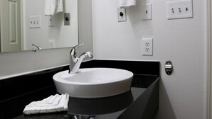 A bathroom with a white sink, a mirror, and a black countertop. There are two towel racks on the wall, and a security camera is mounted on the wall.