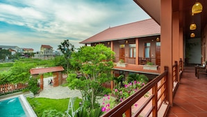 A hotel with a red-tiled roof, a pool, and lush greenery. - Viet Xua Homestay (Ninh Binh)