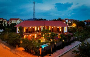 A large, well-lit building with multiple balconies and a swimming pool, surrounded by lush greenery and other residential buildings. - Viet Xua Homestay (Ninh Binh)