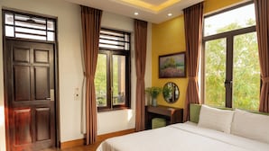 A bedroom with a large bed, wooden flooring, a door, and windows with curtains. - Viet Xua Homestay (Ninh Binh)