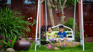 Two children on a white swing set in a garden with a brick wall and potted plants in the background. - Viet Xua Homestay (Ninh Binh)
