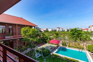 A residential building with a red tiled roof, a swimming pool, and a garden area with a swing set and a red umbrella. - Viet Xua Homestay (Ninh Binh)