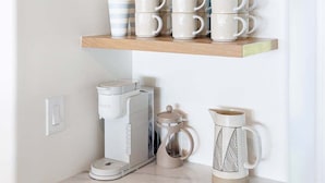 A kitchen with three wooden shelves holding various kitchenware, a coffee maker, and a kettle.