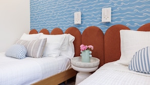 A bedroom with two beds, a wall-mounted light, and a vase with flowers on a side table.