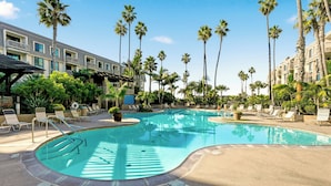 A pool area with lounge chairs, palm trees, and a building with balconies.