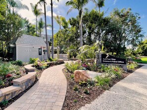 Ein angelegter Eingangsbereich mit einem Weg, der zu einem Gebäude führt, auf dem '999 North Coast Village Entrance & Patrol Office' steht.