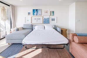A bedroom with a bed, two sofas, a window with curtains, and wall art.
