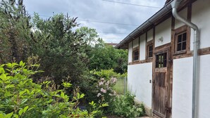 A traditional building with a brick pathway leading to a wooden door, surrounded by lush greenery and a metal fence.