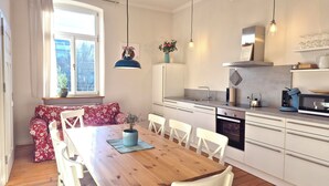 A modern kitchen with white cabinets, a wooden dining table, and a window with curtains.