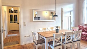 A dining area with a wooden table and white chairs, a mirror above the table, and a door leading to another room.