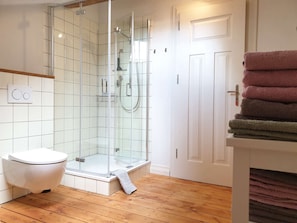A bathroom with a glass-enclosed shower, a toilet, and a stack of towels.