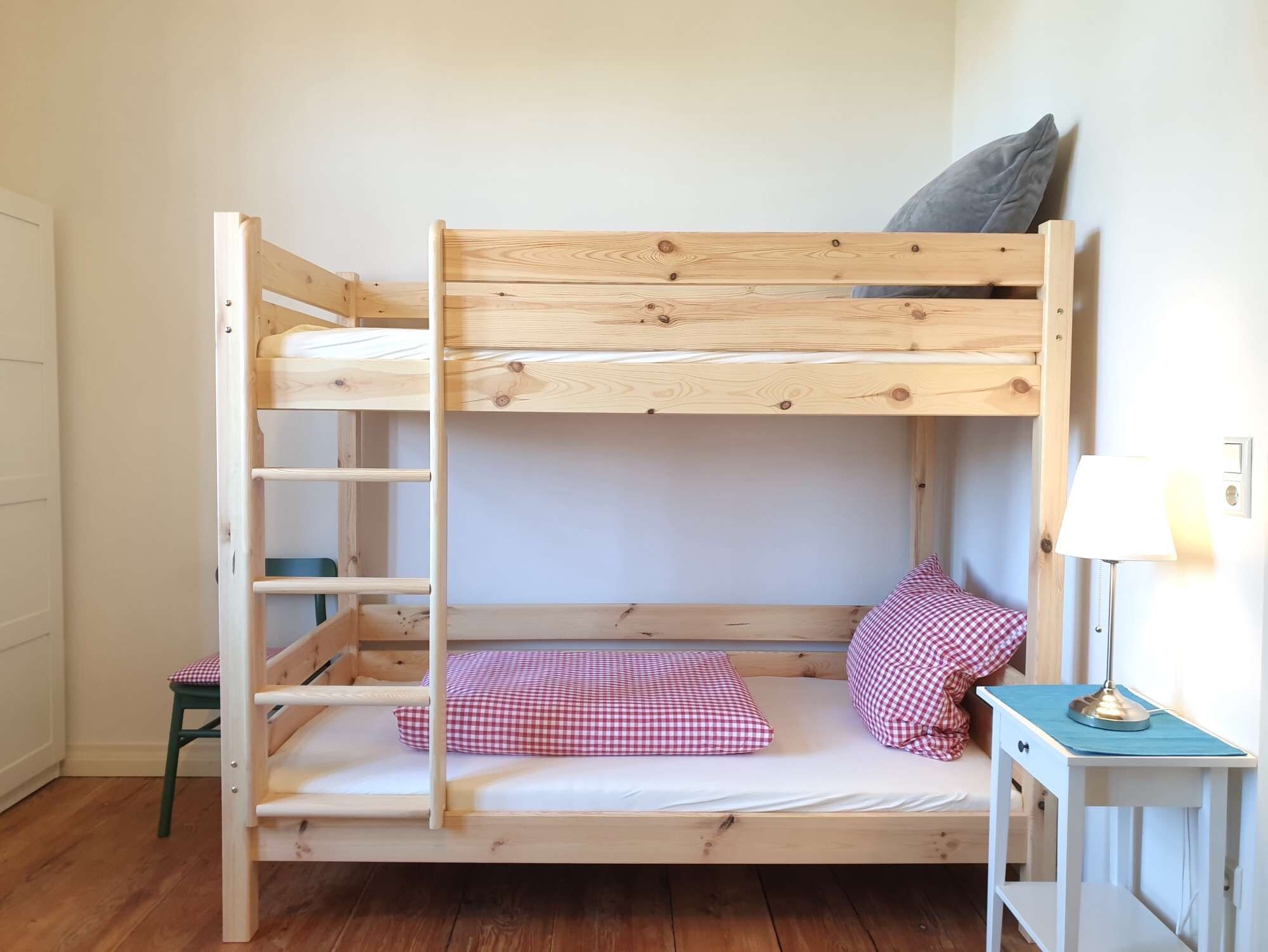 A bunk bed with a ladder, a small stool, a lamp, and a checkered pillow.