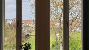 A room with three large windows offering views of a residential area with houses and trees.