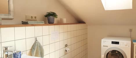 A small, modern bathroom with a sink, toilet, and washing machine.