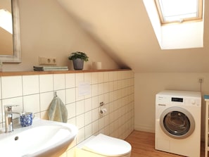 A small, modern bathroom with a sink, toilet, and washing machine.