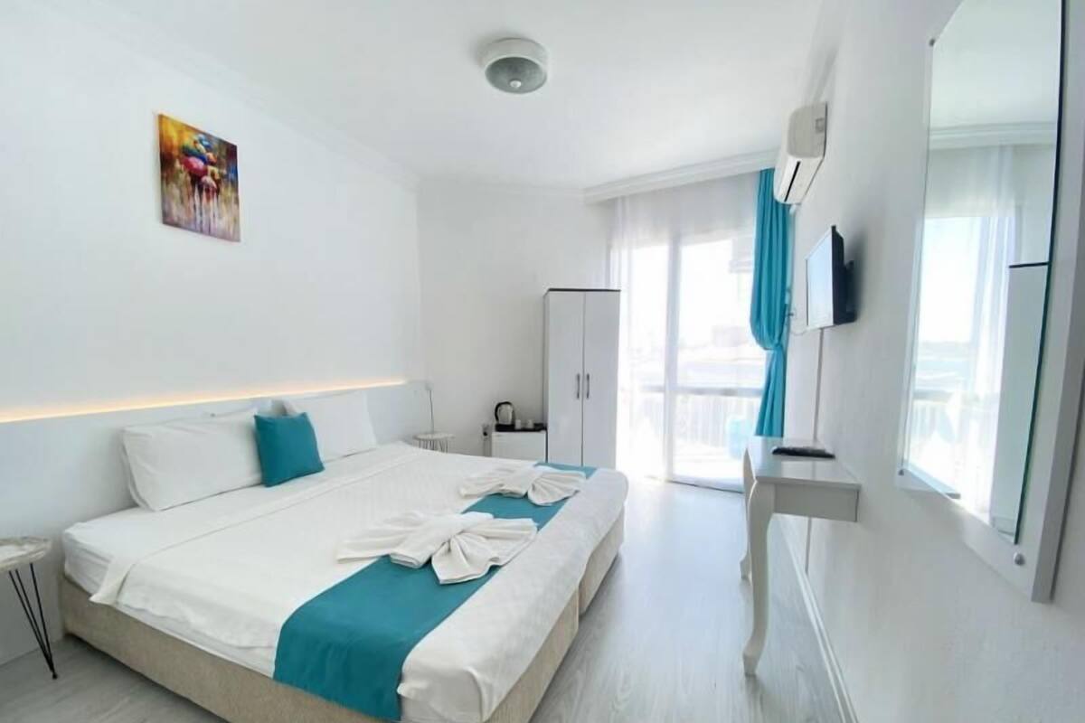 A modern hotel room with a large bed, a desk, a wardrobe, and a television.