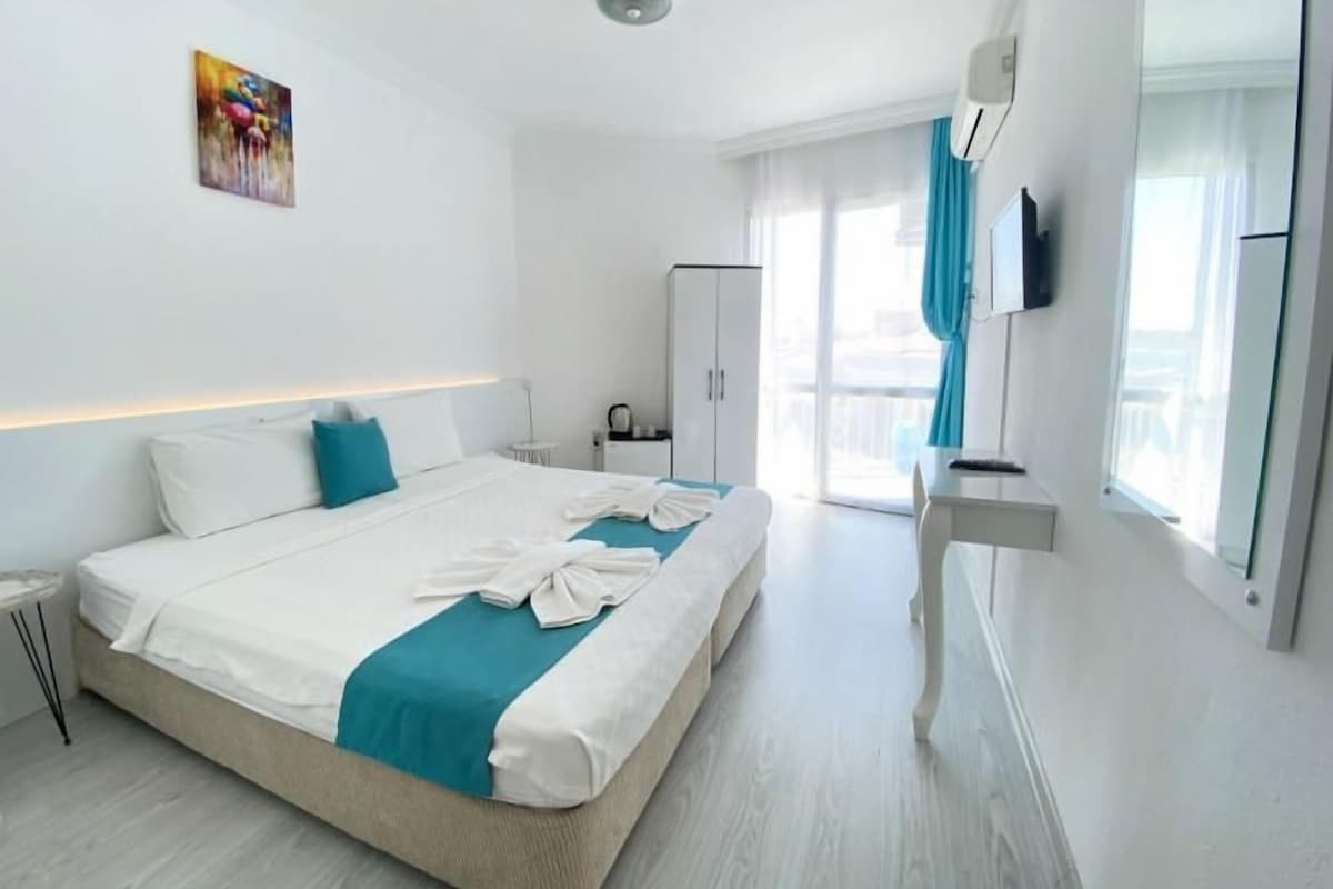 A modern hotel room with a large bed, a desk, a wardrobe, and a television.