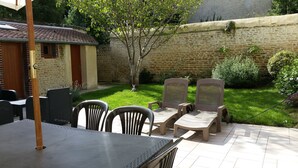 Un patio al aire libre con una mesa y sillas, un pequeño edificio de ladrillo y un muro de piedra.
