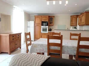 A modern kitchen with wooden cabinets, a dining table with chairs, and a refrigerator. - Spacious house 300 m from the sea. Sheltered garden (Luc-sur-Mer)